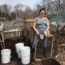 Renee from Kompost Kids standing in front of a pile of compost. She's standing next to three buckets and holding a compost screening tool.