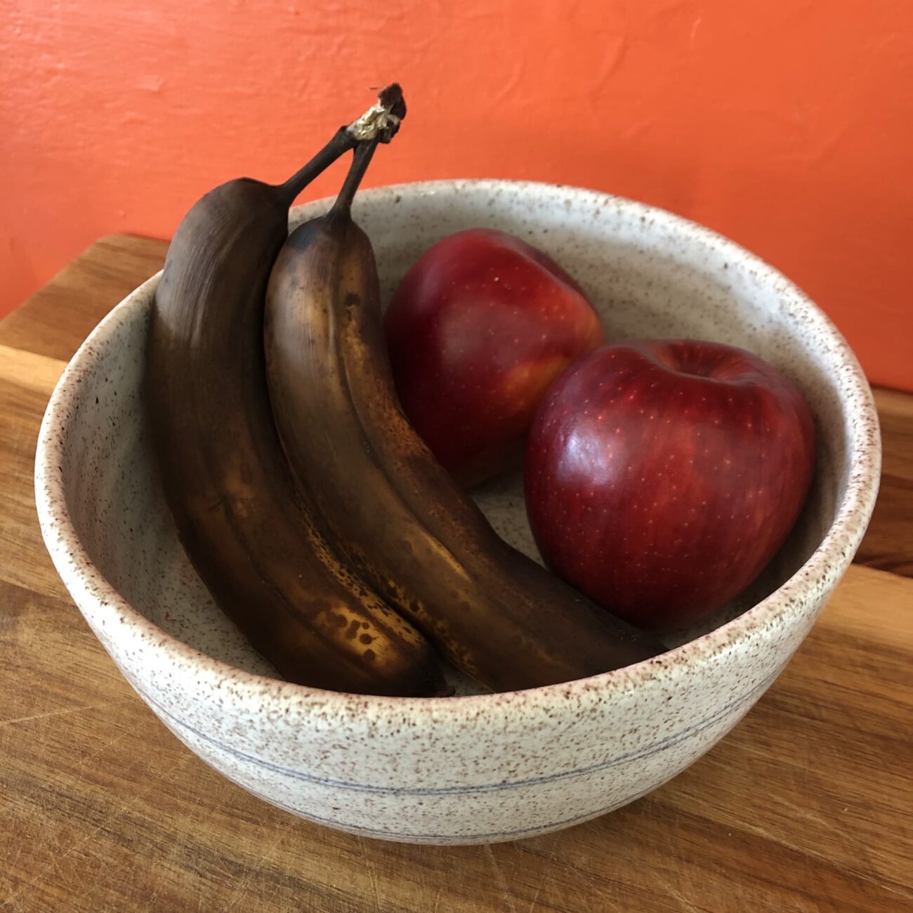Fruit bowl siting on a counter with two overripe bananas and two red apples inside.